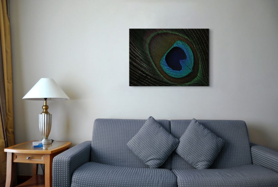 Obraz na płótnie przedstawiający pawie pióro wiszący nad szarą kanapą w kropki