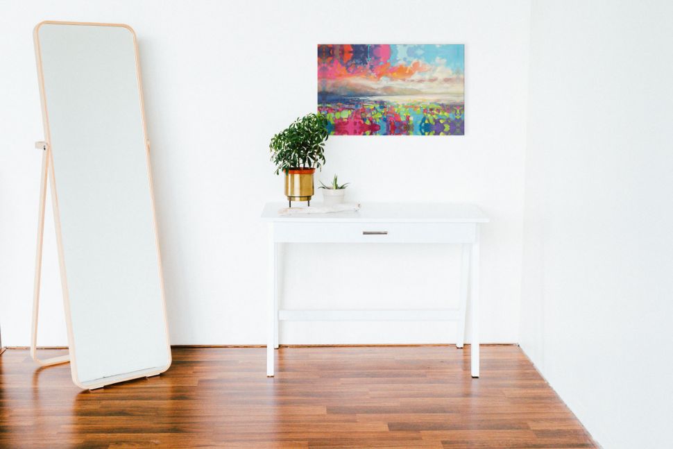 Canvas z barwnym pejzażem wiszący nad białym stolikiem