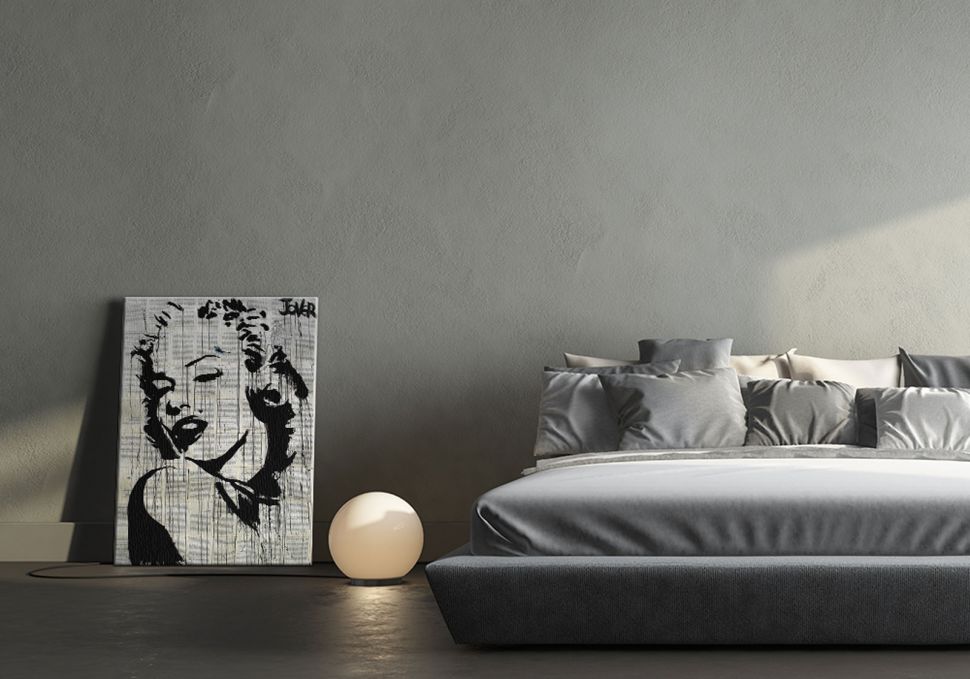 Czarno-biały obraz z Marilyn Monroe postawiony na podłodze obok łóżka i lampki nocnej