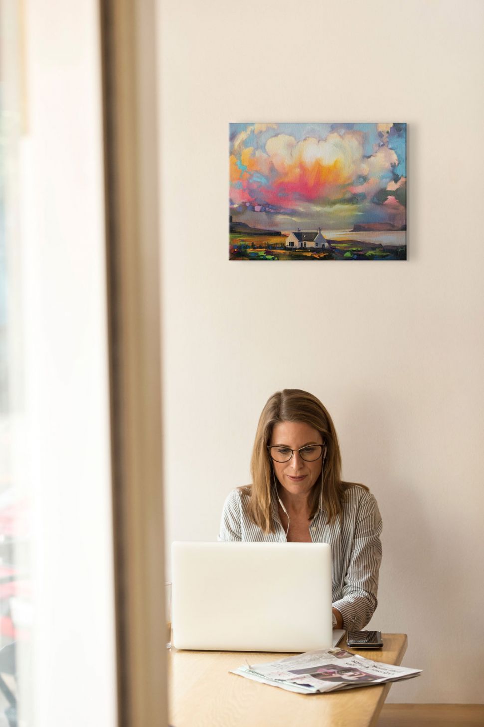 Obraz na płótnie przedstawiający kolorowe niebo nad kościołem powieszony na ścianie nad kobietą siedzącą przed laptopem