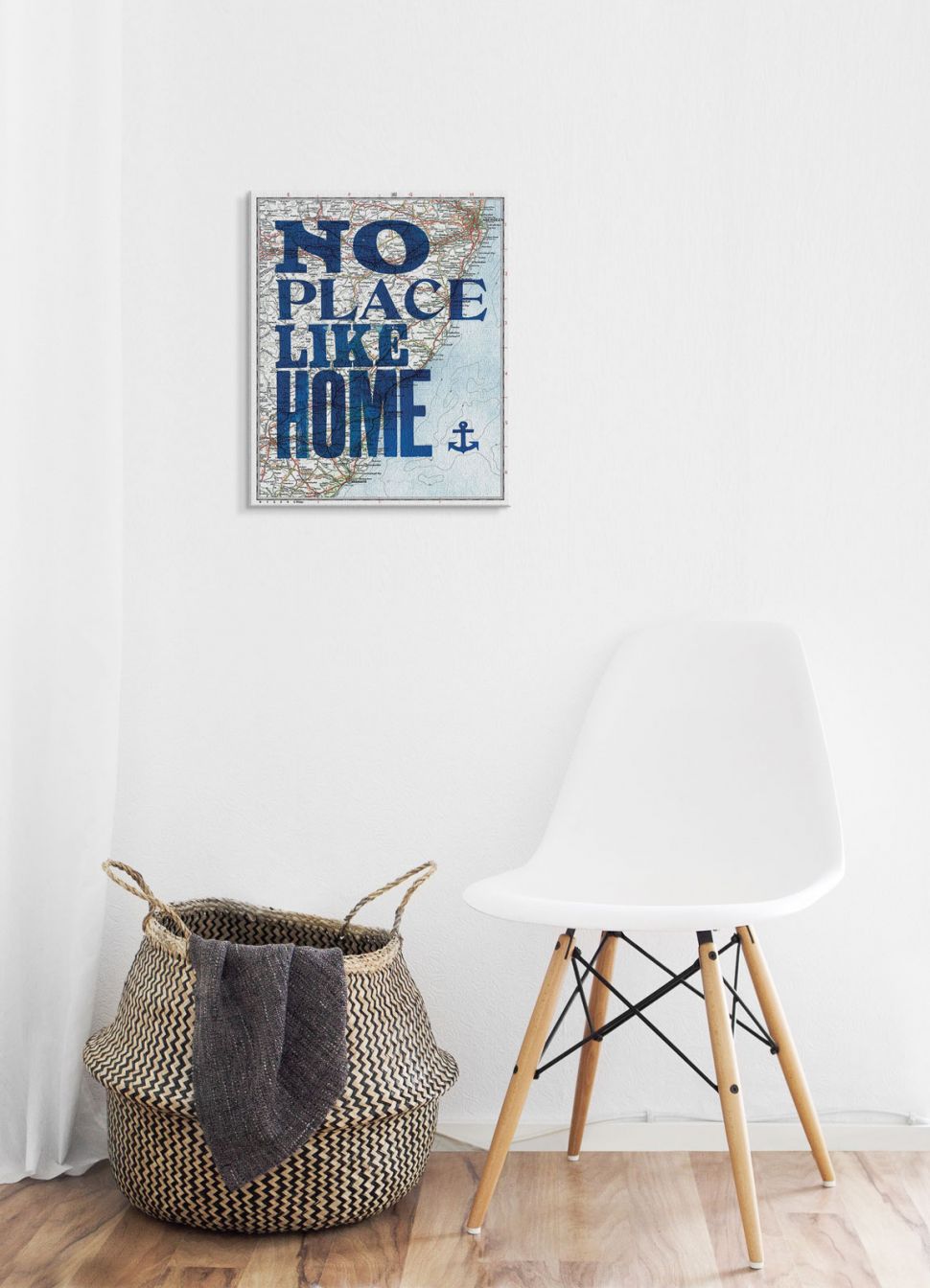 Canvas z napisem no place like home powieszony na białej ścianie nad krzesłem i koszem wiklinowym