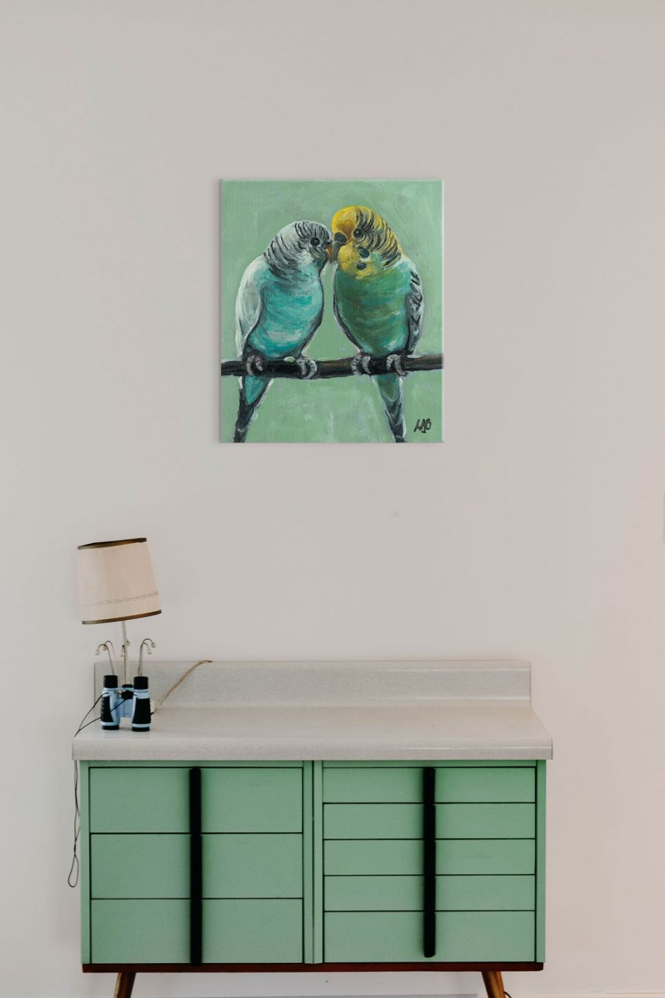 Obraz na płótnie przedstawiający papużki powieszony na ścianie nad komodą z szufladami