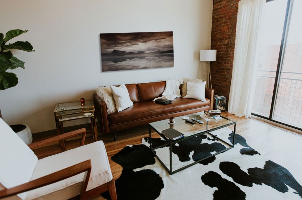 Obraz na płótnie z krajobrazem powieszony w stylowym salonie nad brązową skórzaną kanapą