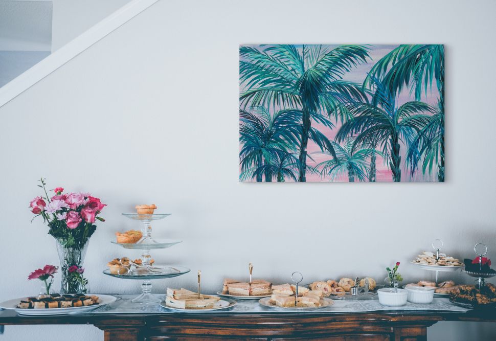 Obraz na płótnie z palmami powieszony na ścianie nad stołem ze słodkościami