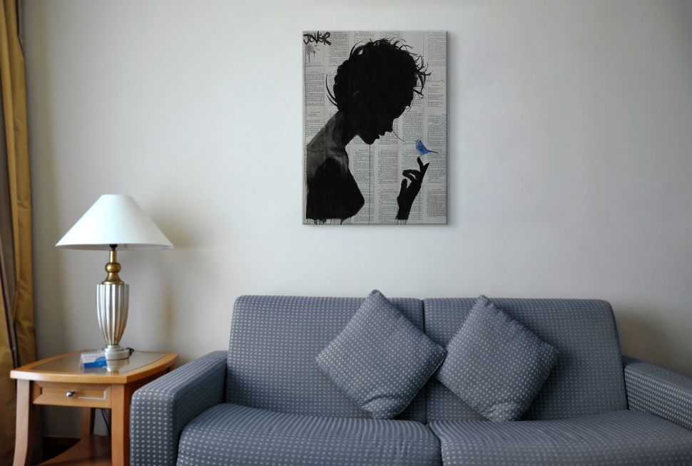 Obraz na płótnie autorstwa Loui Jover przedstawiający kobietę i ptaszka powieszony nad szarą sofą