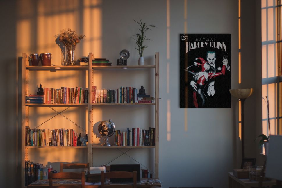Obraz z Harley Quinn i Jokerem powieszony na ścianie obok okna i regału z książkami