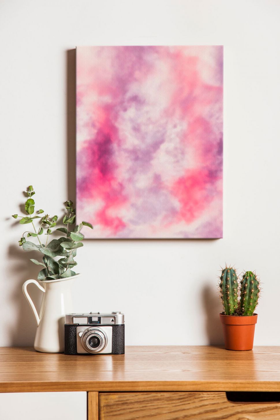 Obraz na płótnie przedstawiający różową abstrakcję powieszony w pokoju na ścianie nad biurkiem z kwiatami