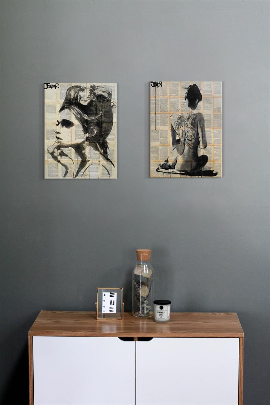 Obrazy Loui Jovera powieszone nad szafką na szarej ścianie