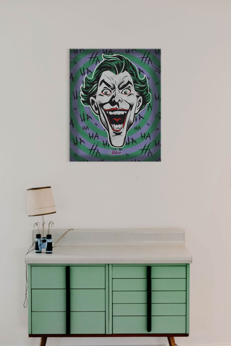 Obraz na płótnie The Joker Hahaha powieszony nad zieloną szafką z lampką