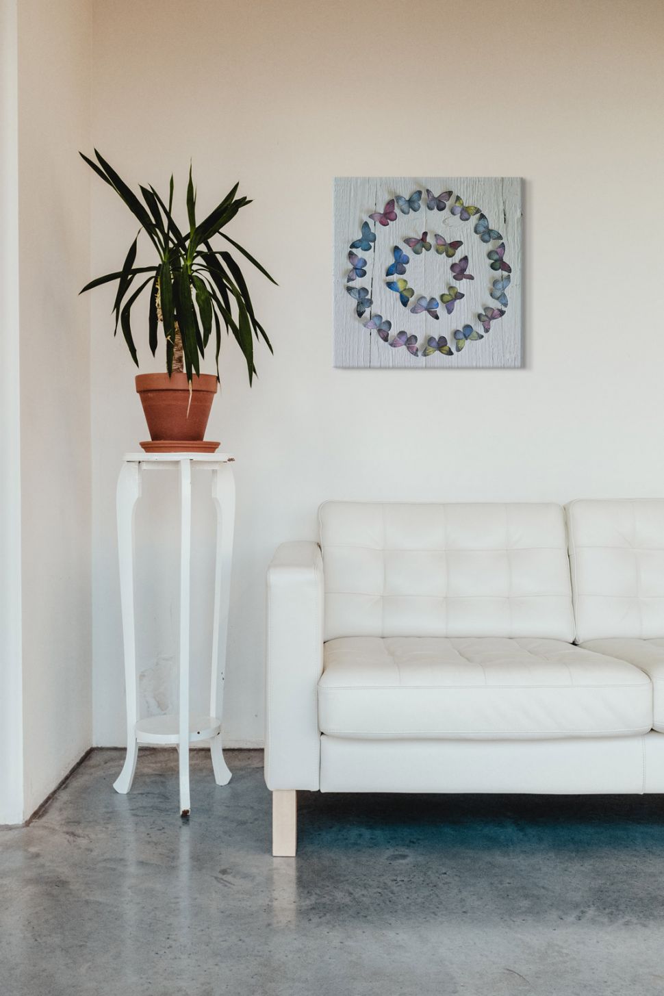 Canvas Koło z motyli autorstwa Howarda Shootera zawieszony w salonie nad białą kanapą obok kwiatka