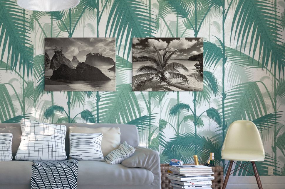 Czarno-biały obraz z widokiem plaży, morza i palmy powieszony w salonie na liściastej fototapecie obok obrazu z plażą