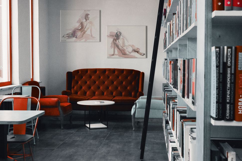 Rysunek nagiej kobiety powieszony w bibliotece nad czerwoną kanapą