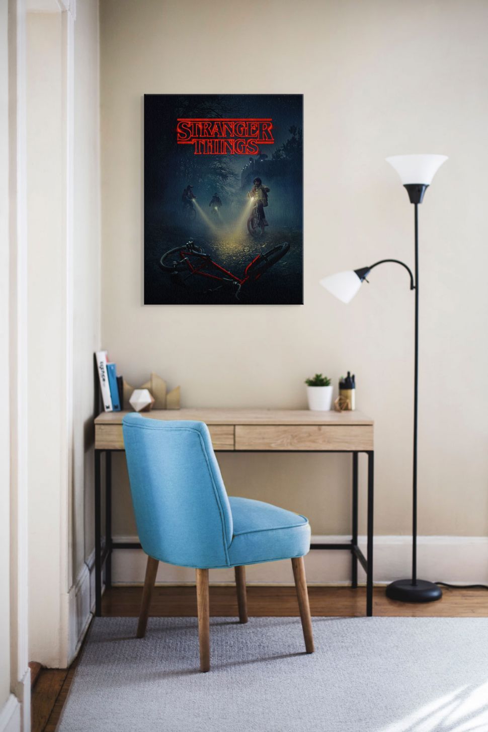 Obraz z chłopcami na rowerach z serialu Stranger Things powieszony w pokoju nastolatka nad biurkiem i niebieskim krzesłem