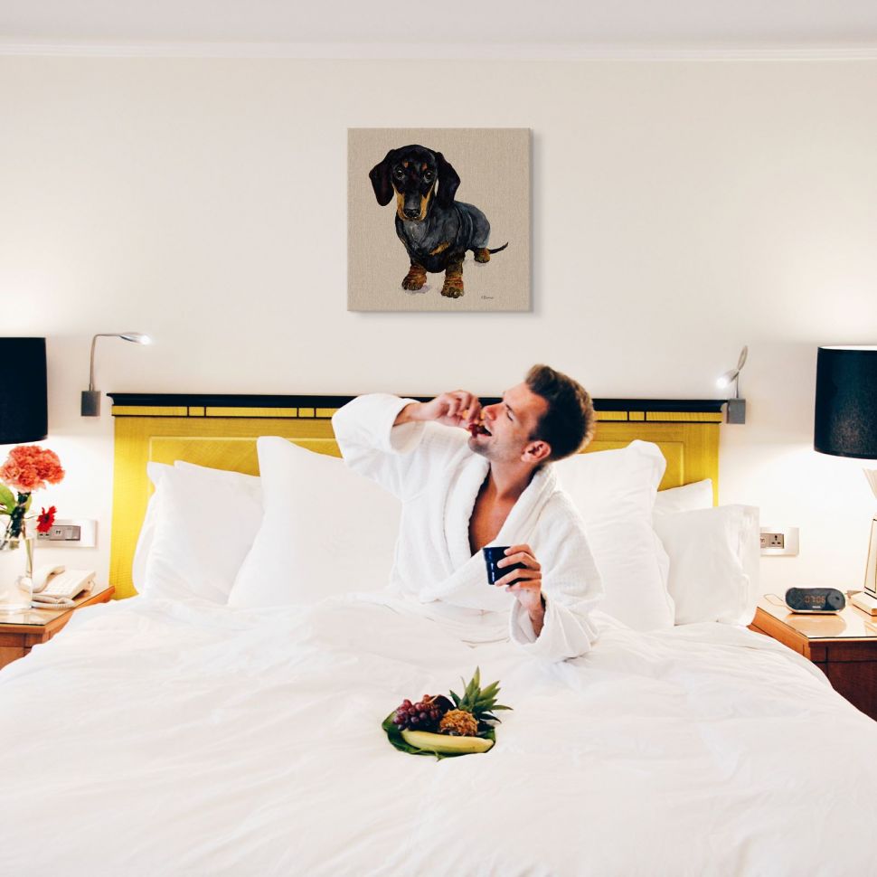 Obraz z czarnym jamnikiem powieszony w sypialni nad żółtym łóżkiem z mężczyzną jedzącym owoce