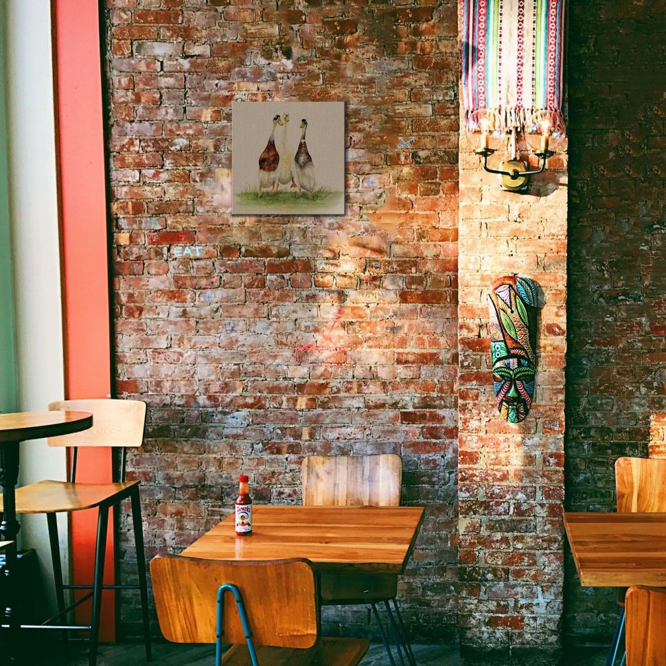 Obraz Trzy gęsi powieszony w barze na ceglanej ścianie nad drewnianym stołem i krzesłem