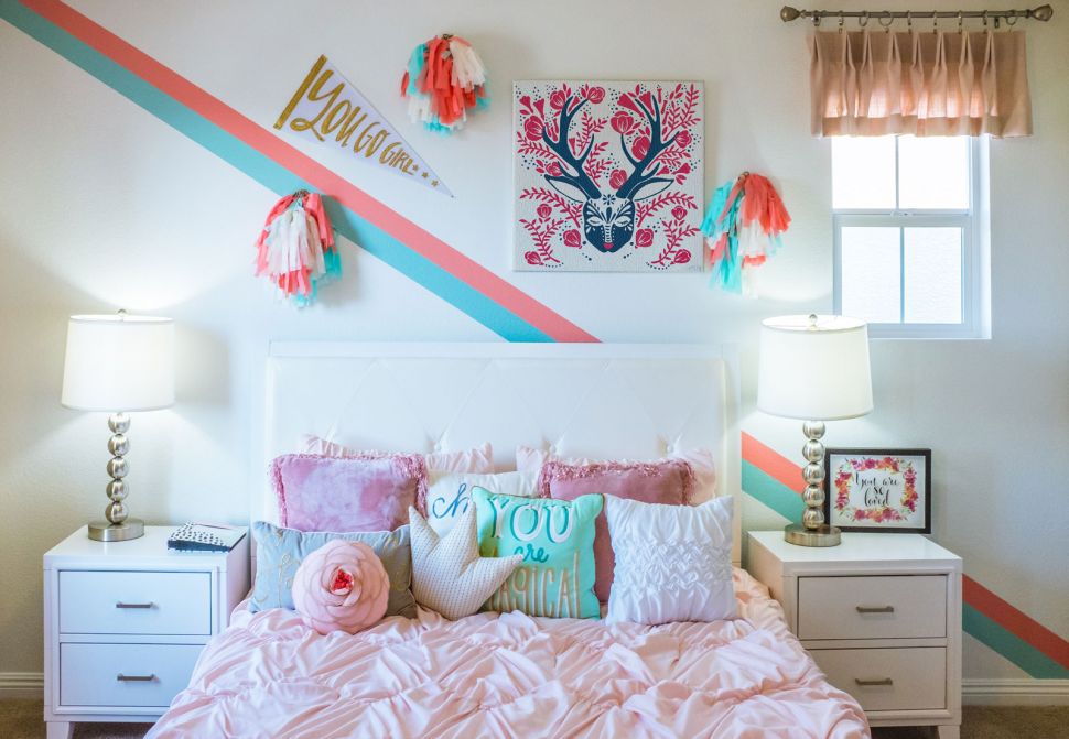Ludowy obraz niebiesko-różowego jelenia zawieszony w pokoju dziewczynki nad łóżkiem z kolorowymi poduszkami