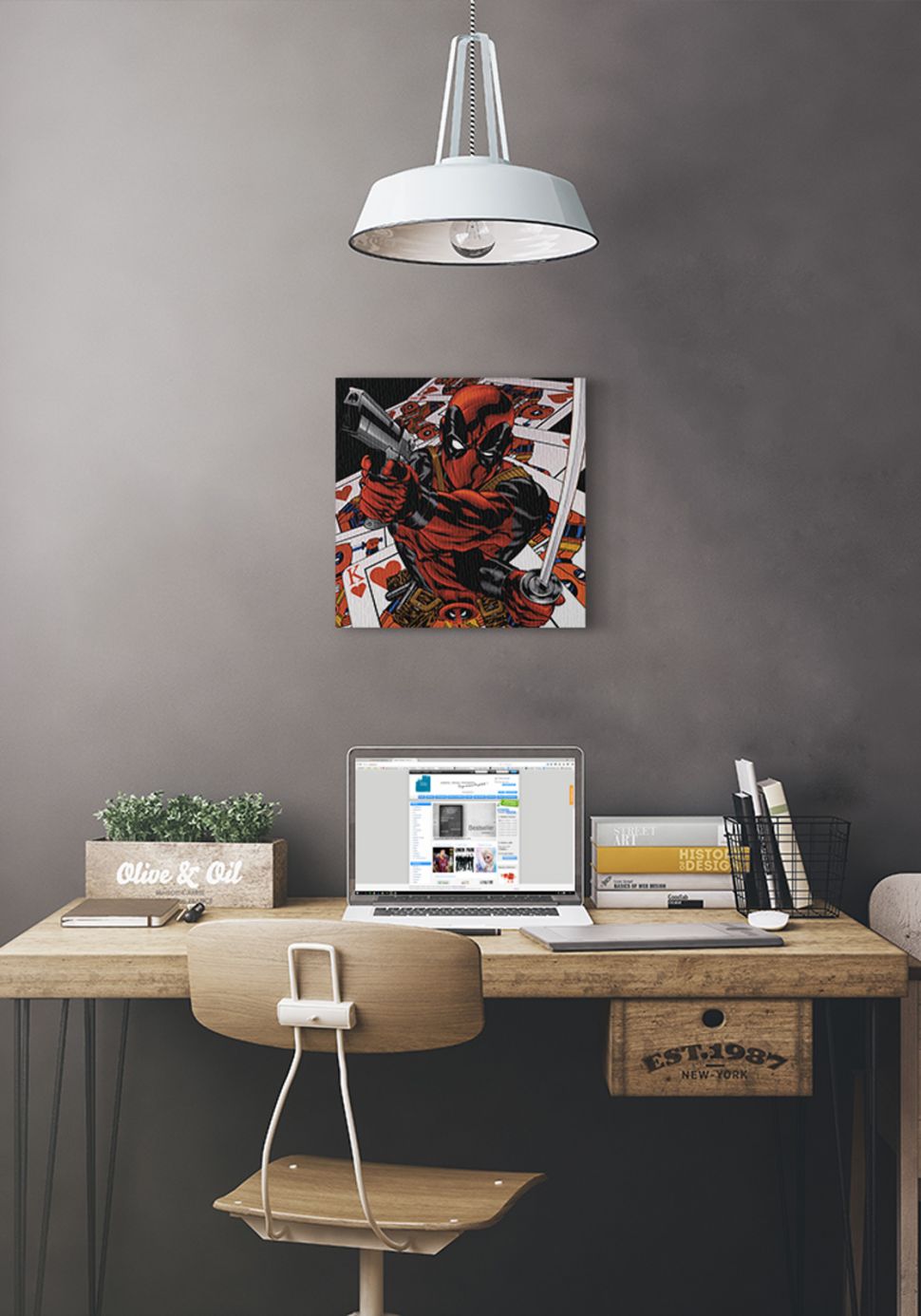 Obraz Deadpoola na tle kart powieszony na szarej ścianie pod białą lampą nad biurkiem z laptopem i książkami