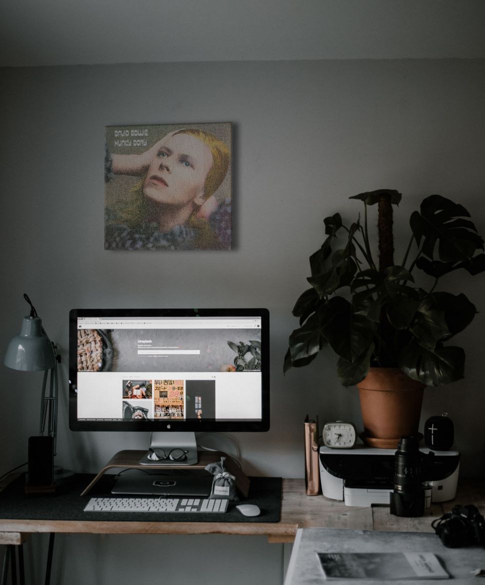 Obraz na płótnie z albumu Hunky Dory Davida Bowie'go powieszony w pokoju nad biurkiem z komputerem, kwiatkiem i lampką