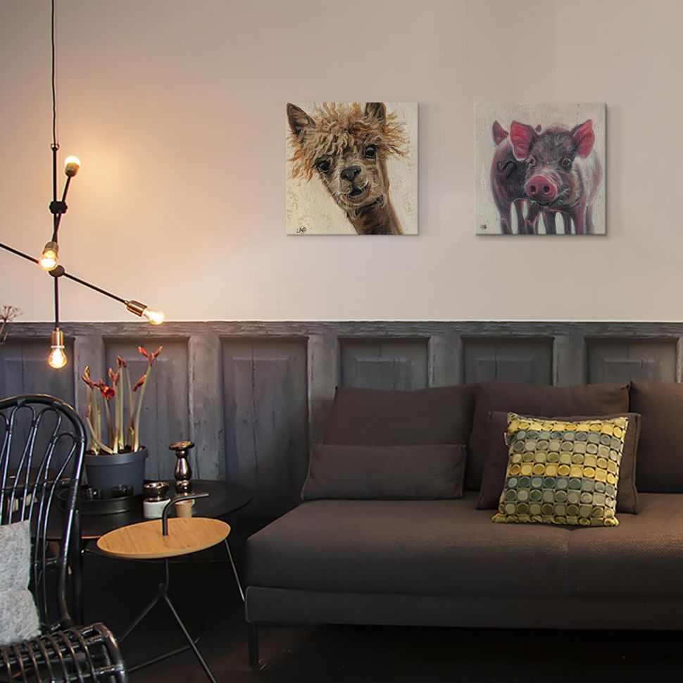 Obraz z lamą powieszony w salonie obok obrazu ze świnką nad brązową kanapa i czarnym stolikiem