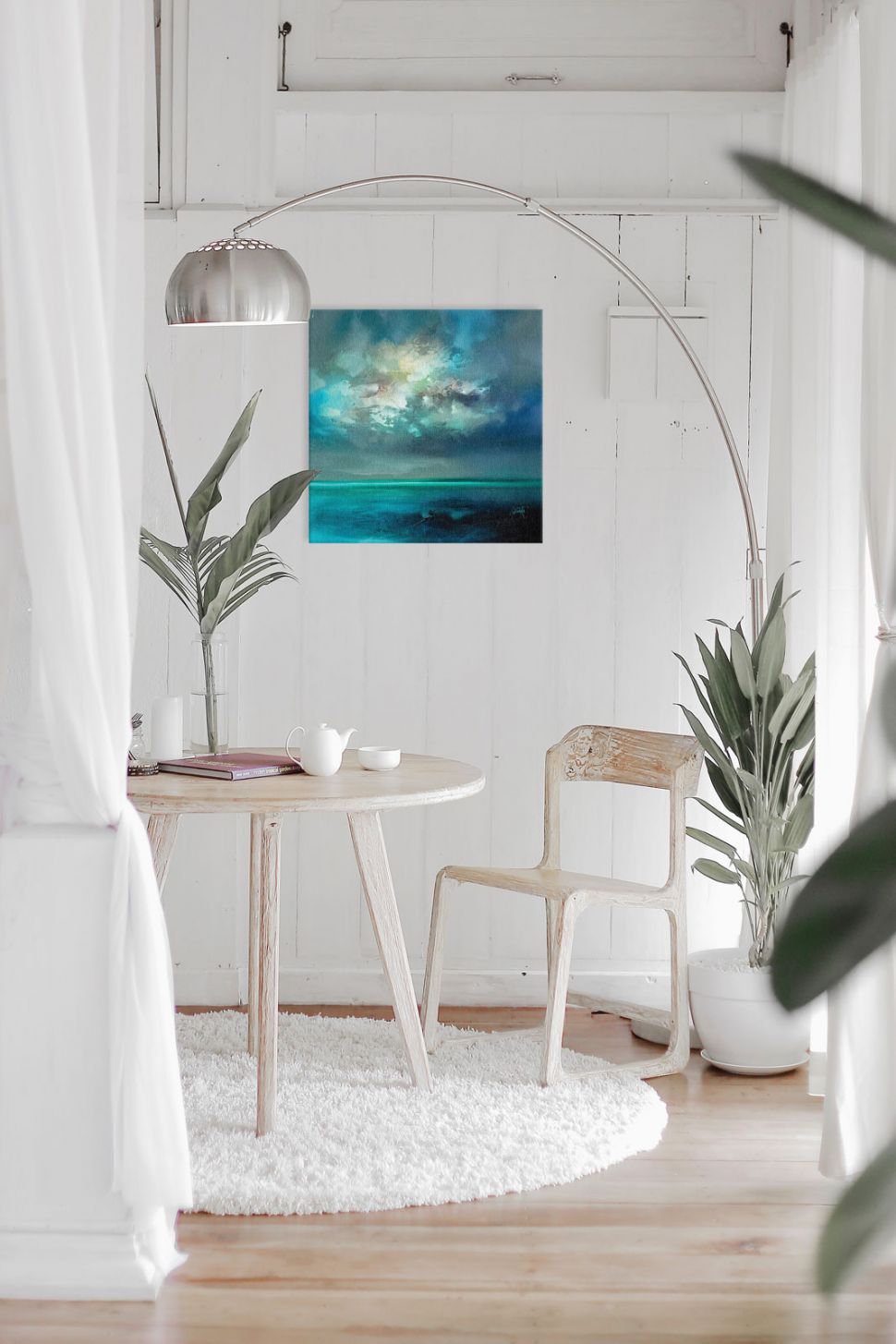 Canvas niebieskiej wyspy zawieszony w salonie nad stolikiem i krzesłem obok kwiatka i lampy