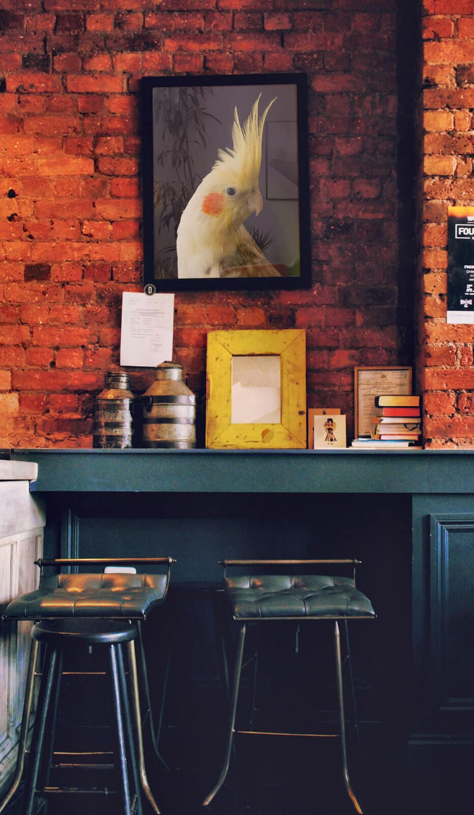 Poster z papugą w żółtmy kolorze powieszony w czarnej ramie na ceglanej ścianie w barze