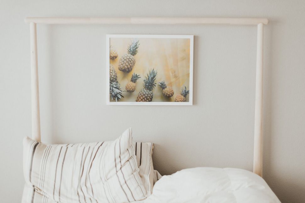 Plakat z Ananasami powieszony nad łóżkiem na białej ścianie