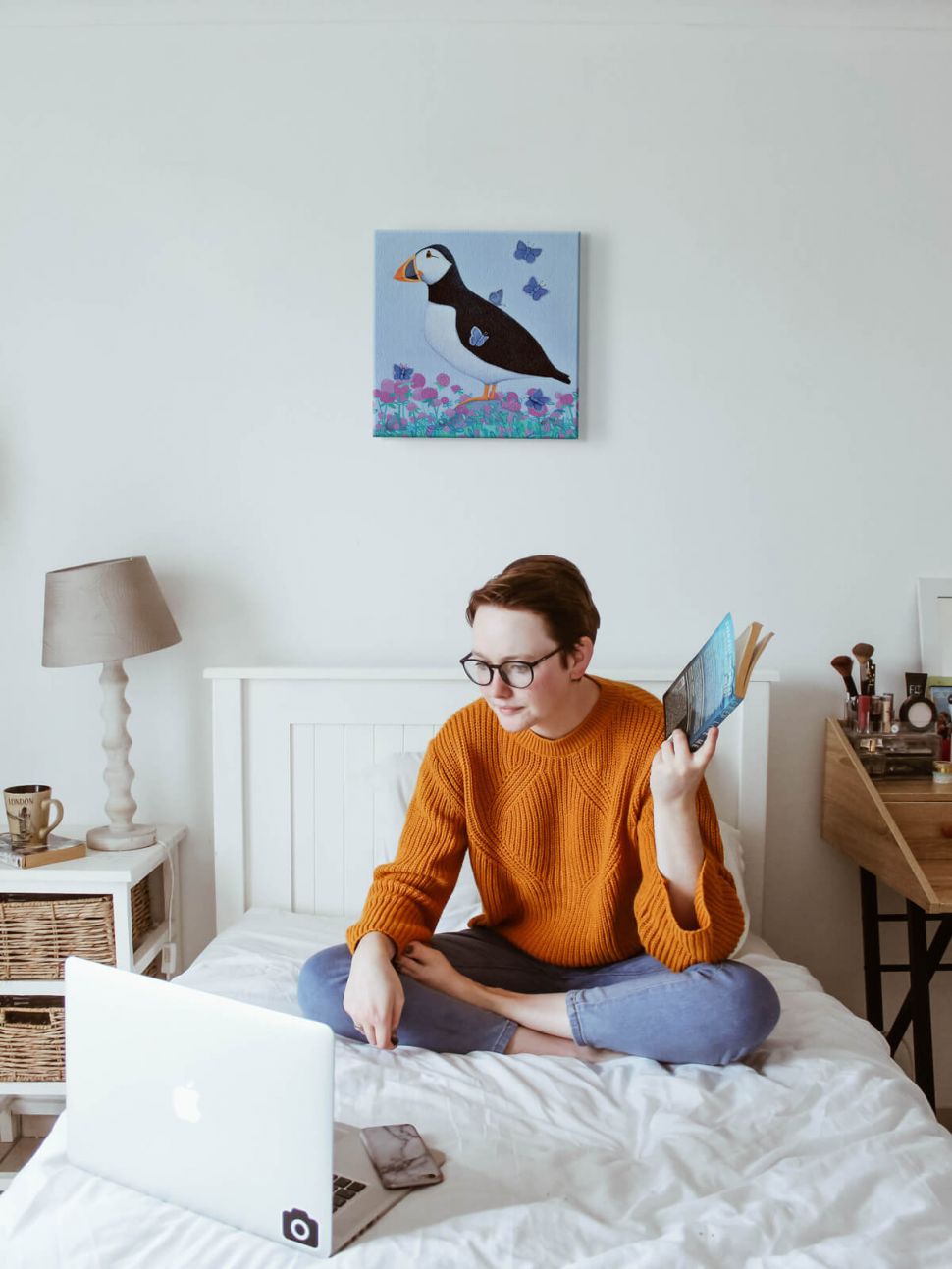 Canvas Puffs of Blue na ścianie w sypialni nad łóżkiem z dziewczyną w pomarańczowym swetrze