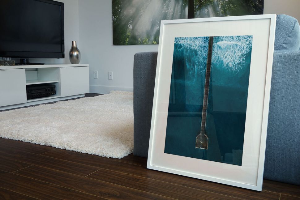 Plakat z molo na wzburzonym morzu w białej ramie postawiony w salonie